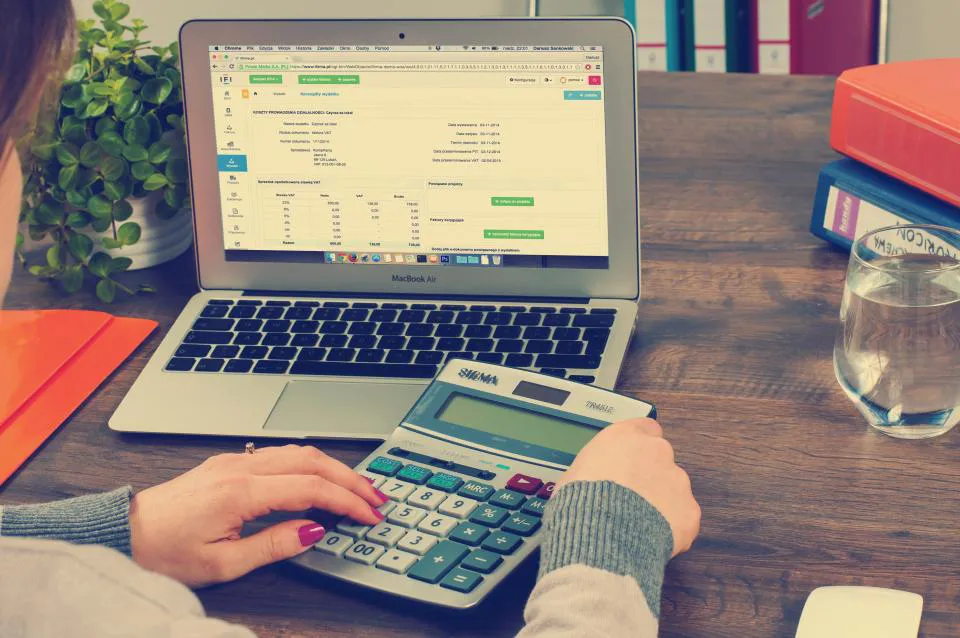 Mains utilisant une calculatrice devant un ordinateur portable